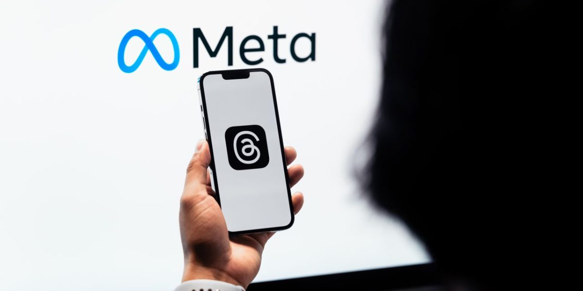 Home Hands holding smartphone with Meta Threads logo on screen, Meta branding in background.
